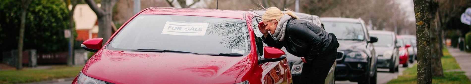 Woman looking into a red car window labeled as for sale